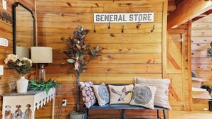A wooden interior with a sign reading 'GENERAL STORE,' a bench with decorative pillows, a vase with flowers, and a wall-mounted lamp. - Hideaway Haven – A Private Retreat on 100 Acres (Marion)