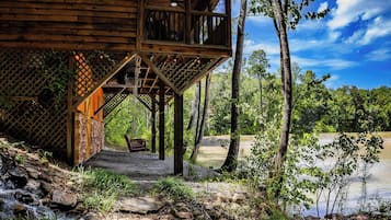 A wooden cabin with a balcony overlooking a river, surrounded by trees.