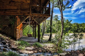 A wooden cabin with a balcony overlooking a river, surrounded by trees. - Hideaway Haven – A Private Retreat on 100 Acres (Marion)
