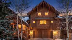 Un grand chalet en bois avec une entrée centrale, des murs en pierre et un escalier extérieur abrité.
