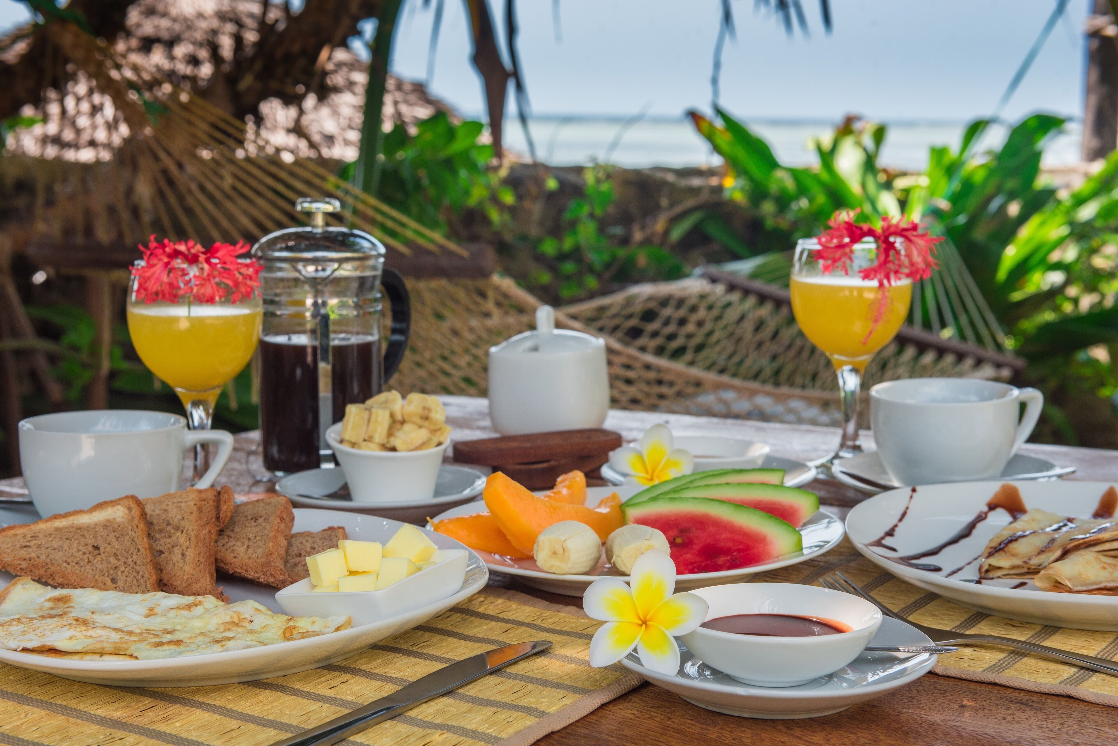 Een ontbijtsetting met toast, eieren, fruit en drankjes op een tafel met uitzicht op de oceaan.