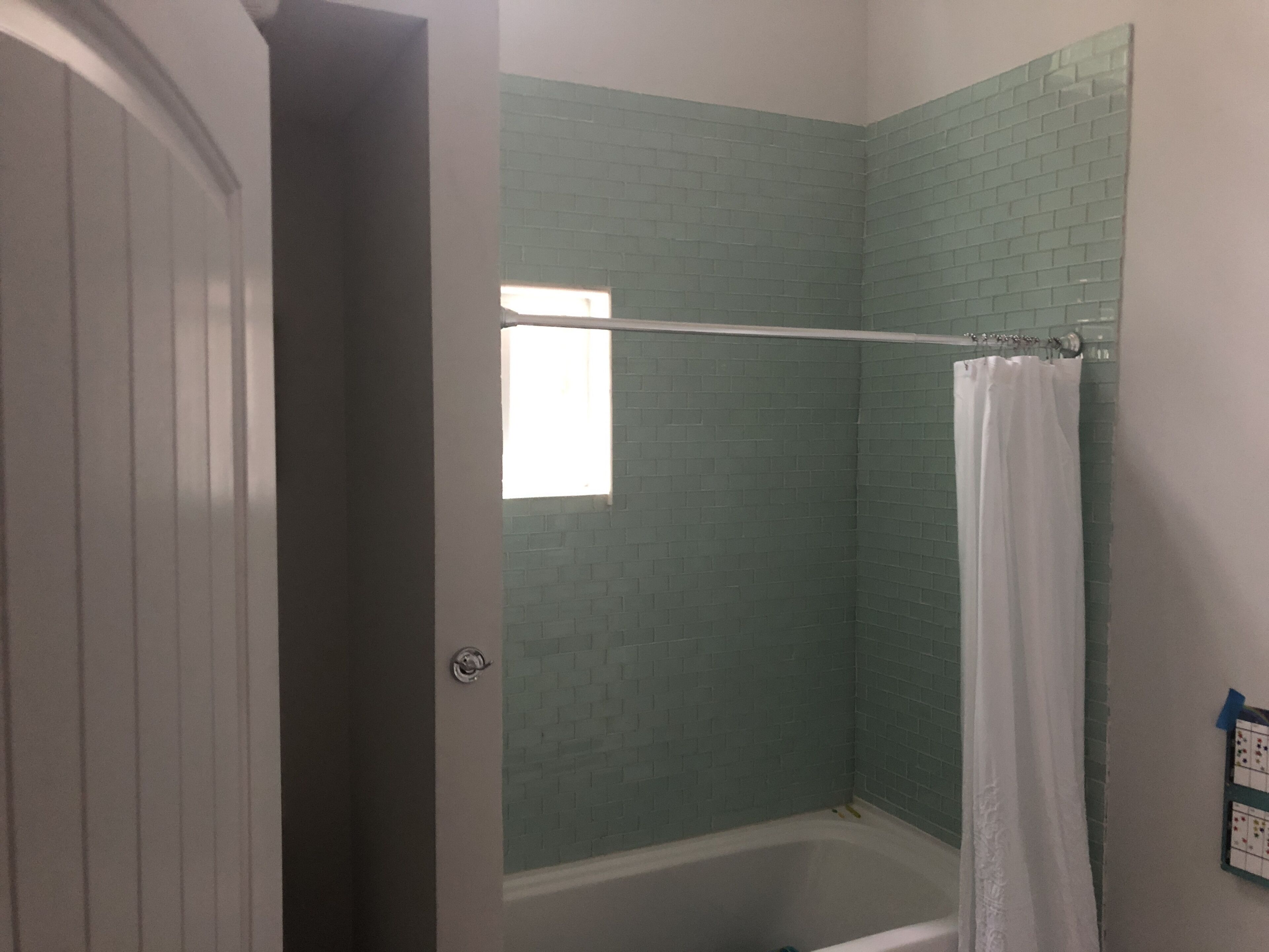 A bathroom with a shower, a white bathtub, and a green-tiled wall.