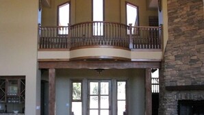 A spacious living area with a stone fireplace, a balcony with a wooden railing, and a kitchen in the background. - Spectacular Torreon Mountain Estate (Show Low)