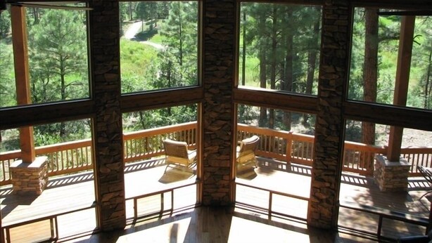 A room with large windows overlooking a forested area. There is a wooden deck with outdoor furniture. - Spectacular Torreon Mountain Estate (Show Low)