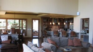 A spacious living area with a large sofa set, a coffee table, and a fireplace. There is a kitchen area with wooden cabinets and a stone countertop visible through an open doorway. - Spectacular Torreon Mountain Estate (Show Low)
