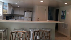 A kitchen with white cabinets, a refrigerator, a sink, and a bar area with stools. - Peaceful, Beach-front Escape in Orange Beach! 3/3 with pool and more! (Orange Beach)