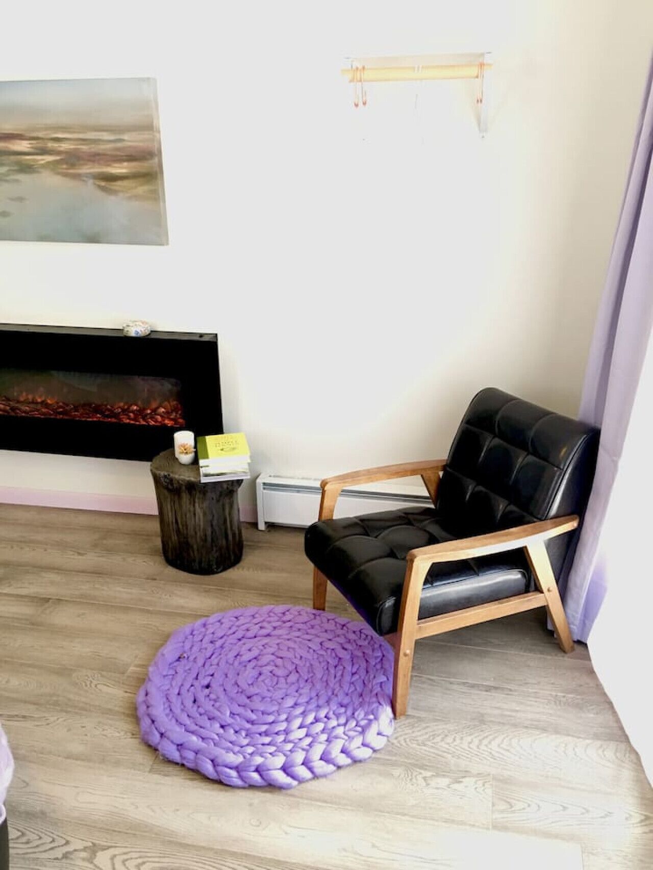 Un salón con un sillón de cuero negro, un tapete redondo morado, una mesita de madera y una chimenea.