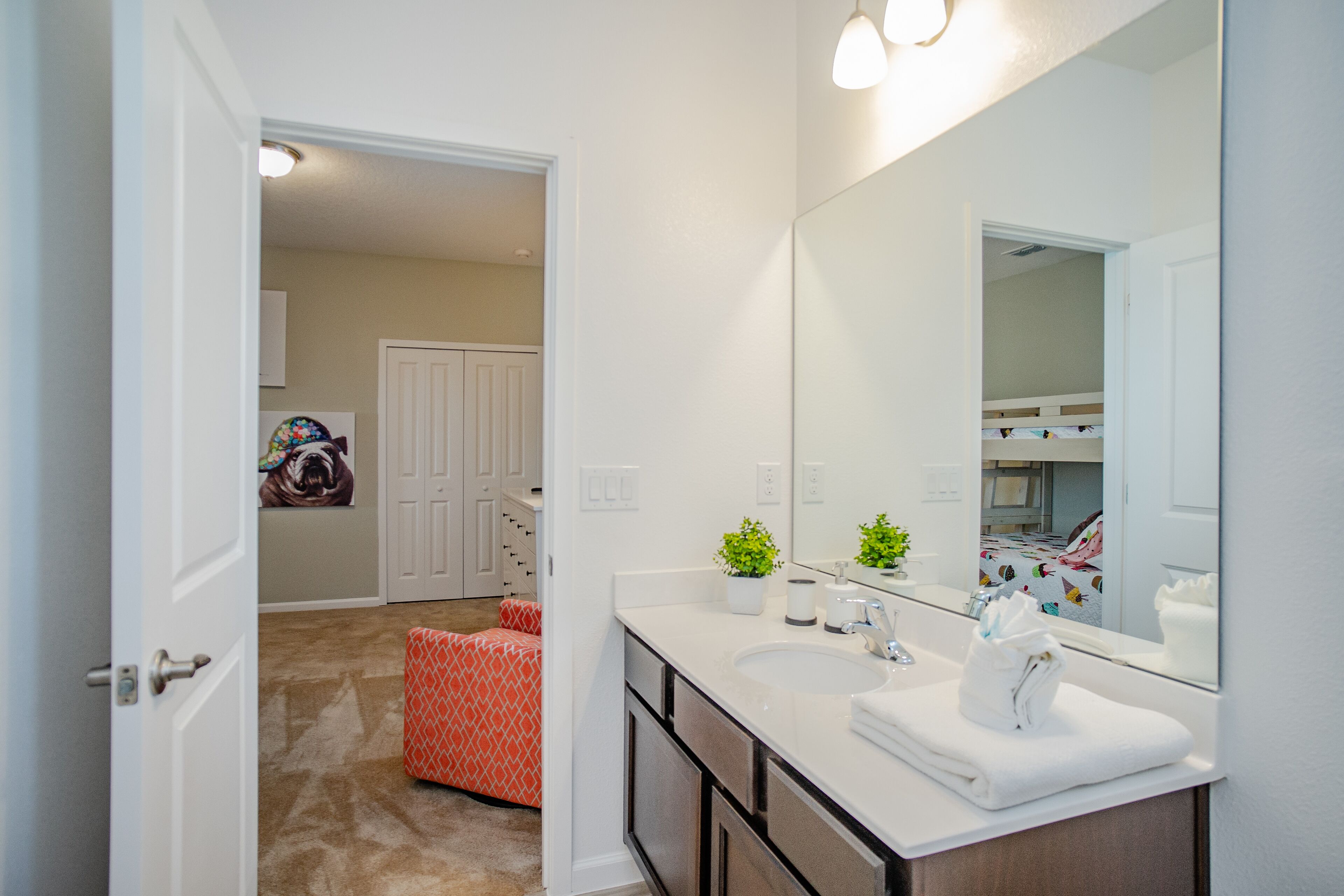 A bathroom with a white sink, mirror, and towel rack. There is a red chair in the corner and a small plant on the counter.