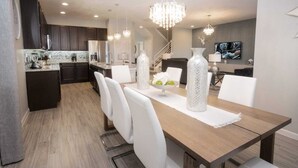 Une cuisine moderne avec des meubles de couleur sombre, un îlot central et un coin repas comprenant une table en bois et des chaises blanches.