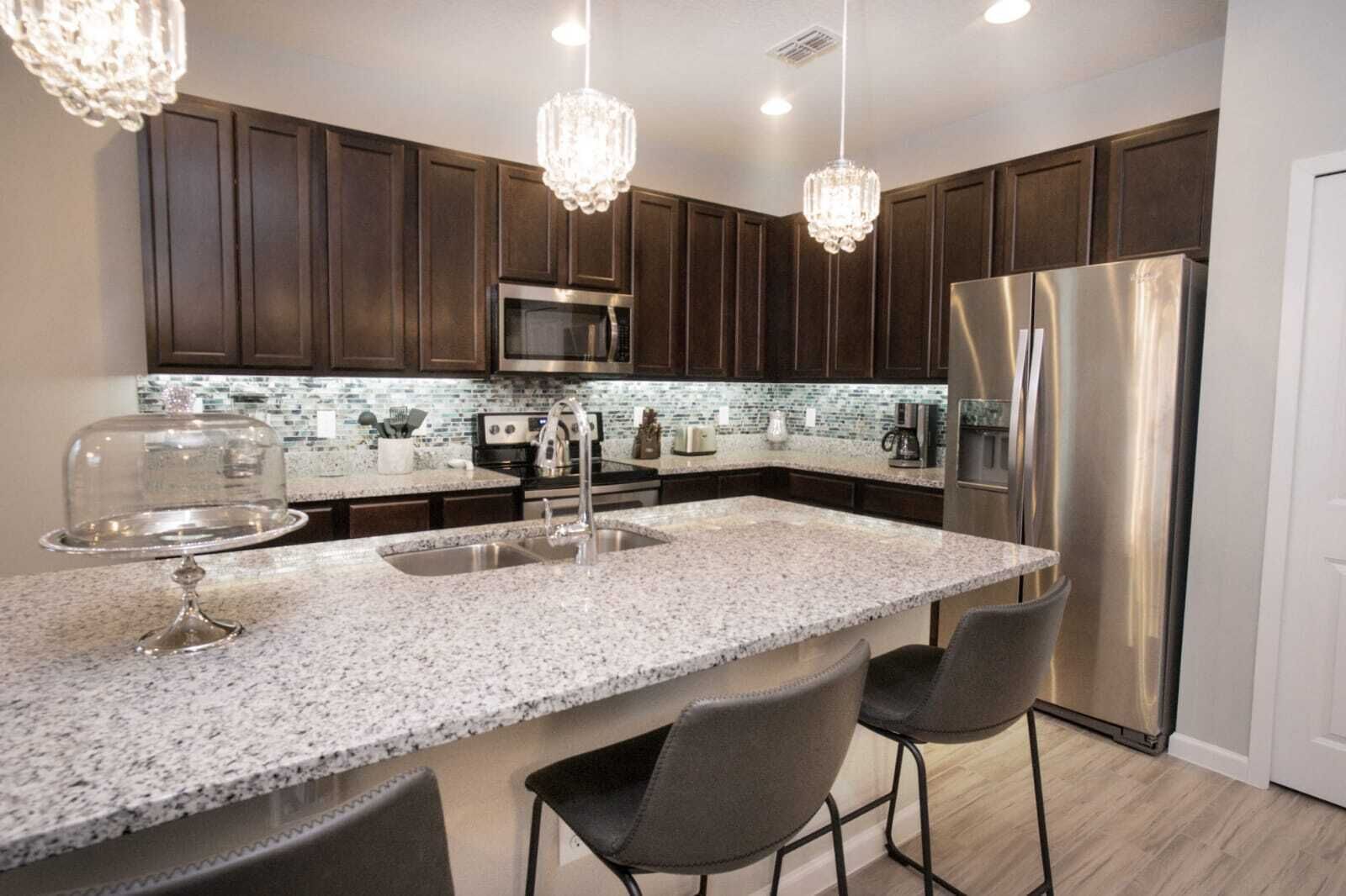 Una cocina moderna con armarios de madera oscura, electrodomésticos de acero inoxidable y encimeras de granito, además de taburetes de bar.
