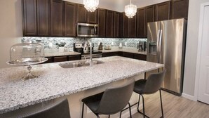 Une cuisine moderne avec des meubles de couleur bois foncé, des appareils électroménagers en acier inoxydable, des plans de travail en granit et des tabourets de bar.
