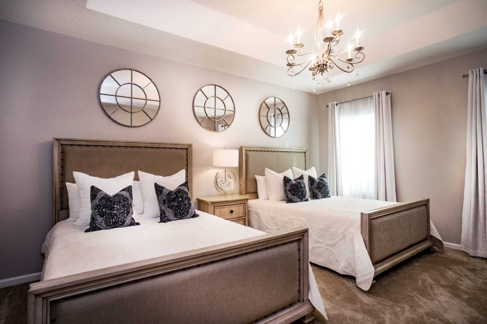 A hotel room with two beds, a chandelier, and wall mirrors.