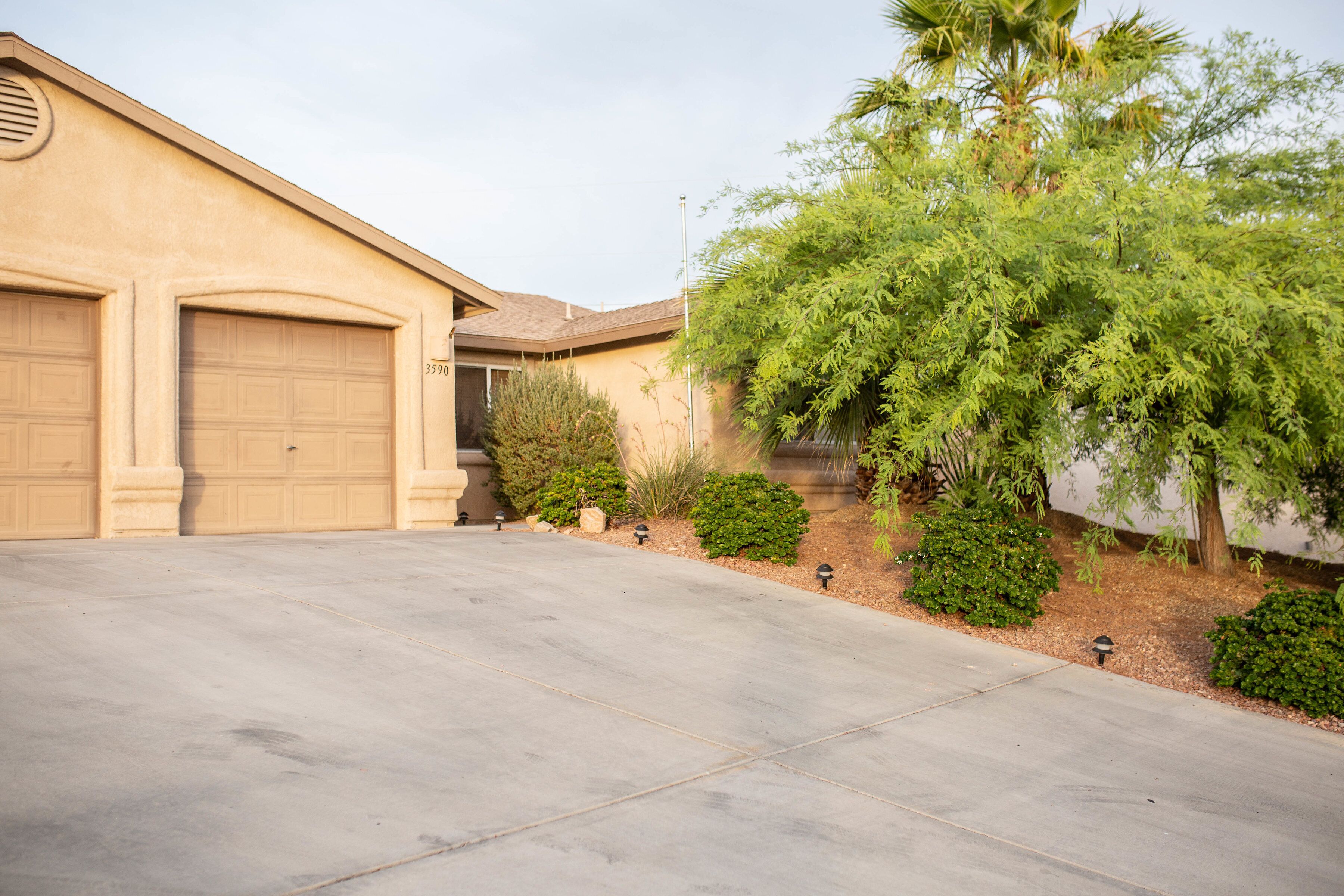 A residential driveway with two garage doors, a well-maintained lawn, and various shrubs and trees.