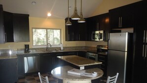 A kitchen with dark cabinets, a stainless steel refrigerator, a microwave, a stove, and a sink. There is a window providing natural light and a checkered floor pattern. - Modern Home Secluded in the Mountains With Breathtaking Views in Divide CO (Divide)