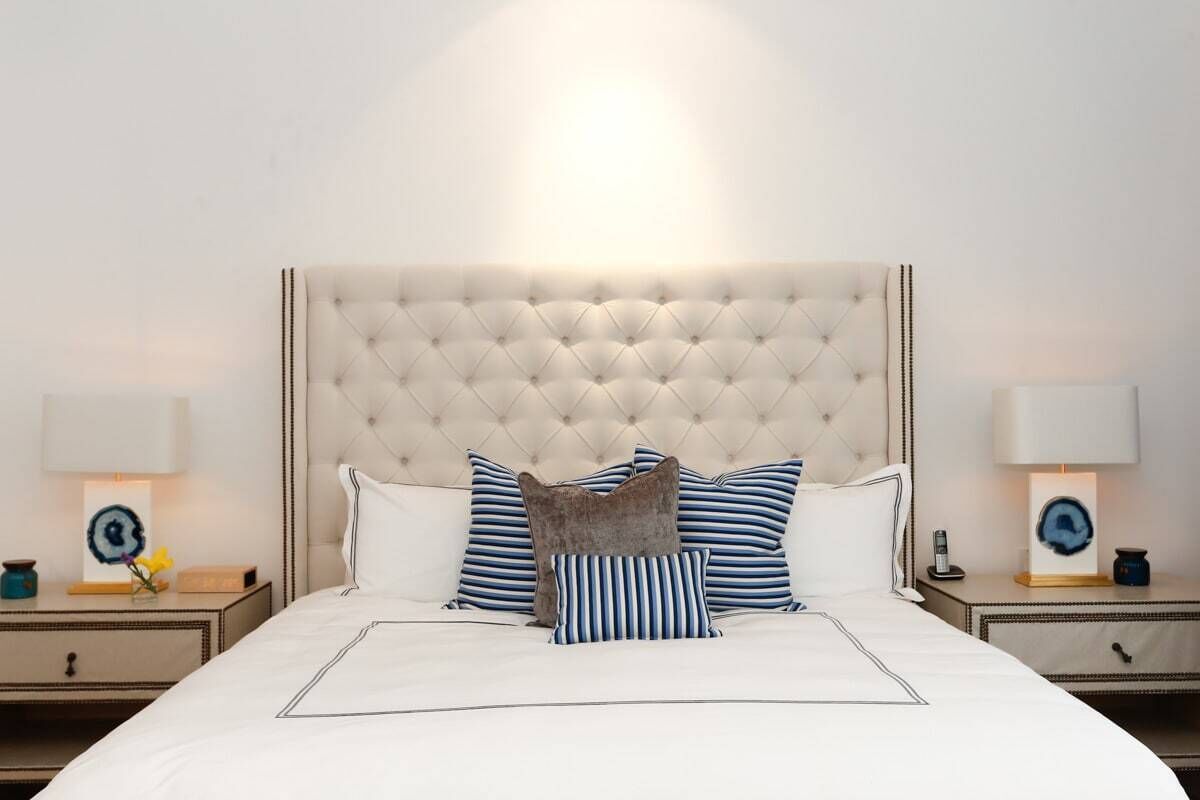 A neatly made bed with a tufted headboard, striped pillows, and bedside tables with lamps and small decorative items.