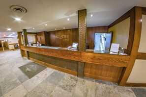 A reception desk with a wooden finish, a digital kiosk, and a sign reading "GLACIER LODGE".