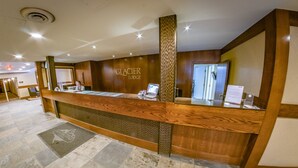 Un comptoir d’accueil avec un revêtement en bois, un kiosque numérique et une enseigne indiquant « GLACIER LODGE ».
