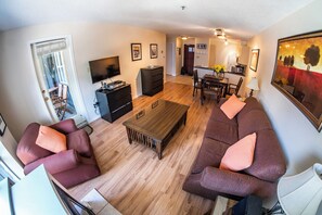 A living room with a sofa set, a coffee table, and a TV. There is a dining area with a table and chairs.