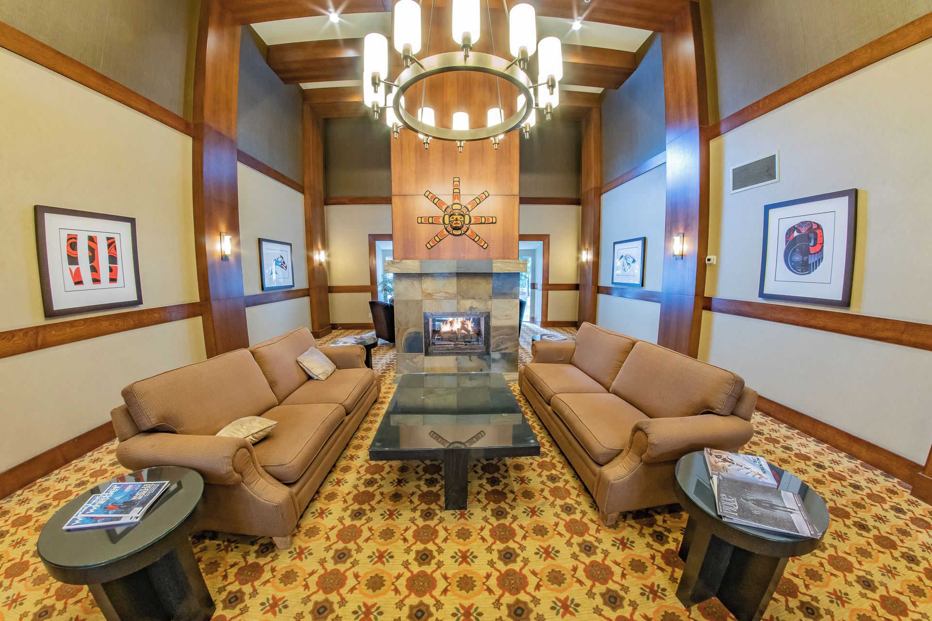 A lobby with two sofas facing a fireplace, a chandelier, and framed artwork on the walls.