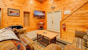 A cozy log cabin interior with a wooden floor, a sofa, a table, a mounted TV, and a fire extinguisher. - Moonbeams & Star Dreams... A Spectacular Mountain View (Gatlinburg)