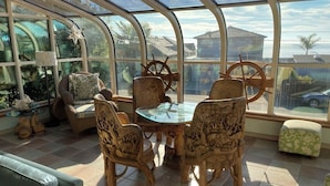 A sunroom with a curved glass ceiling, a round glass table, and wooden chairs with animal carvings. - Opal Cliff Beach House (Pleasure Point)