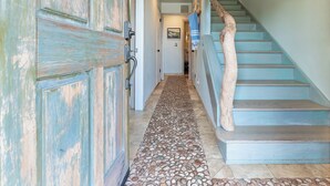 A hallway with a stone-tiled floor, a wooden door, and a staircase with blue steps and a wooden handrail. - Opal Cliff Beach House (Pleasure Point)