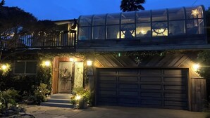 A house with a glass-enclosed upper level, a wooden front door, and a garage. - Opal Cliff Beach House (Pleasure Point)