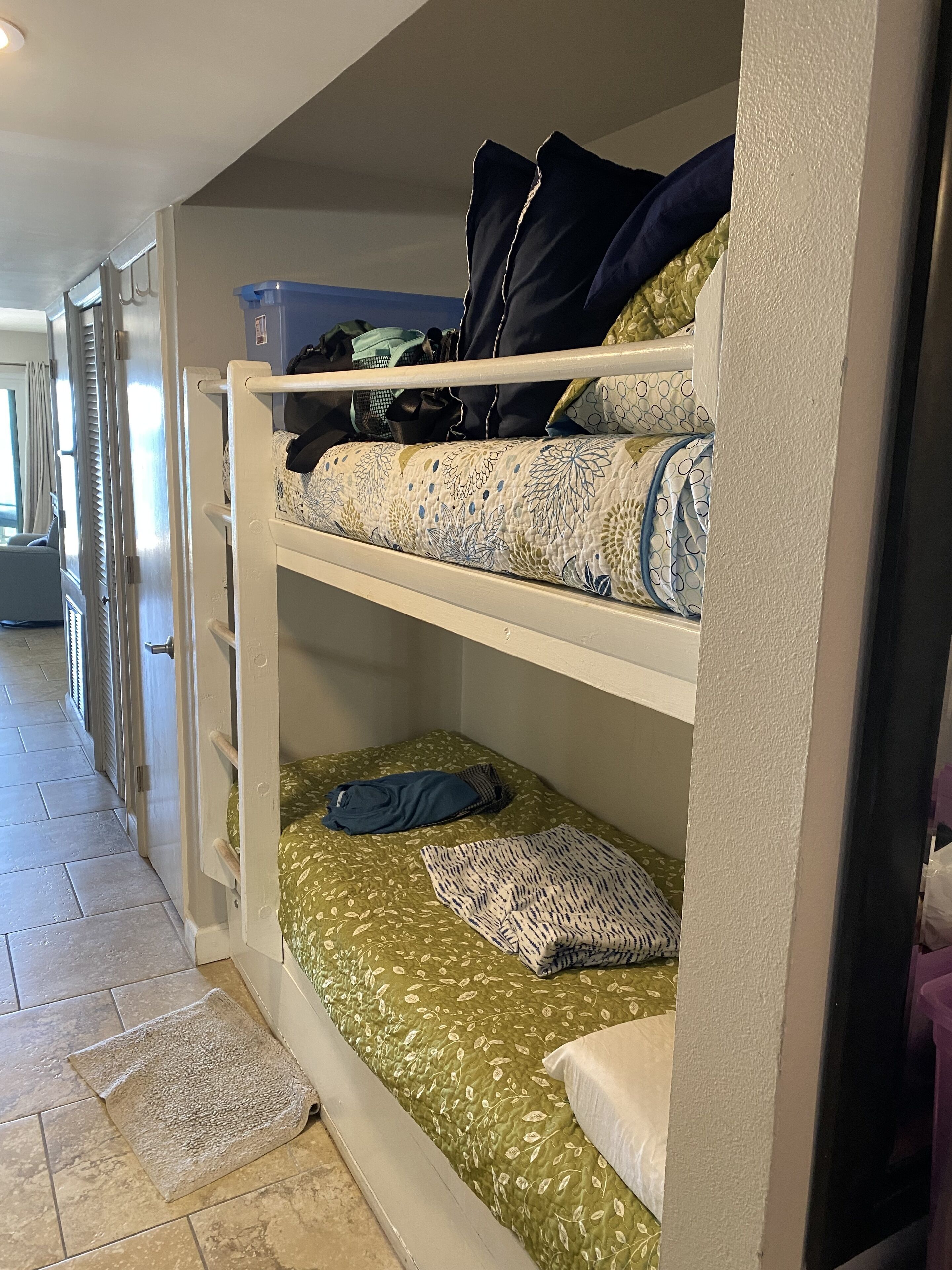 A bunk bed with a green leaf-patterned bedspread, a white pillow, and a blue blanket.