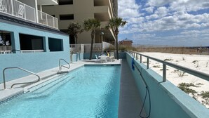 Ein Pool mit Metallgeländer, ein Sandstrand im Hintergrund und ein Gebäude mit Balkonen.