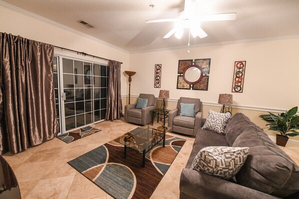 A living room with a sofa, two armchairs, a coffee table, a floor lamp, and a potted plant.
