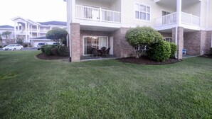 A multi-story building with a brick facade, white balconies, and a small patio area with chairs and a table. - Beautiful private end unit! Featuring 2b/2b near swimming pool.   (Myrtle Beach)