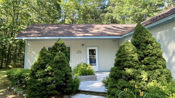 A single-story house with a front porch, surrounded by trees. - Convenient in town location (Beaver Island)