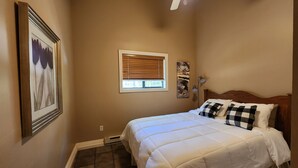 A bedroom with a bed, a ceiling fan, a window with blinds, and a wall-mounted artwork. - Convenient in town location (Beaver Island)
