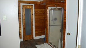 A bathroom with wooden paneling, a glass shower enclosure, and a white door. - Convenient in town location (Beaver Island)