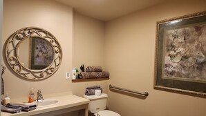 A bathroom with a sink, toilet, and a mirror with an ornate frame. There is a towel rack with towels and a shelf with toiletries. - Convenient in town location (Beaver Island)