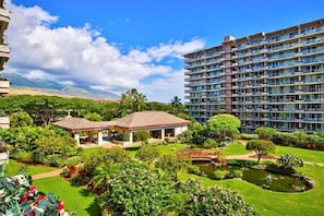 Un hotel con un edificio grande, una estructura más pequeña con techo y un jardín cuidado con un estanque.