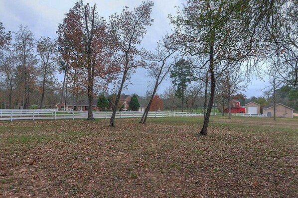 A rural landscape with trees, a white fence, and farm buildings.