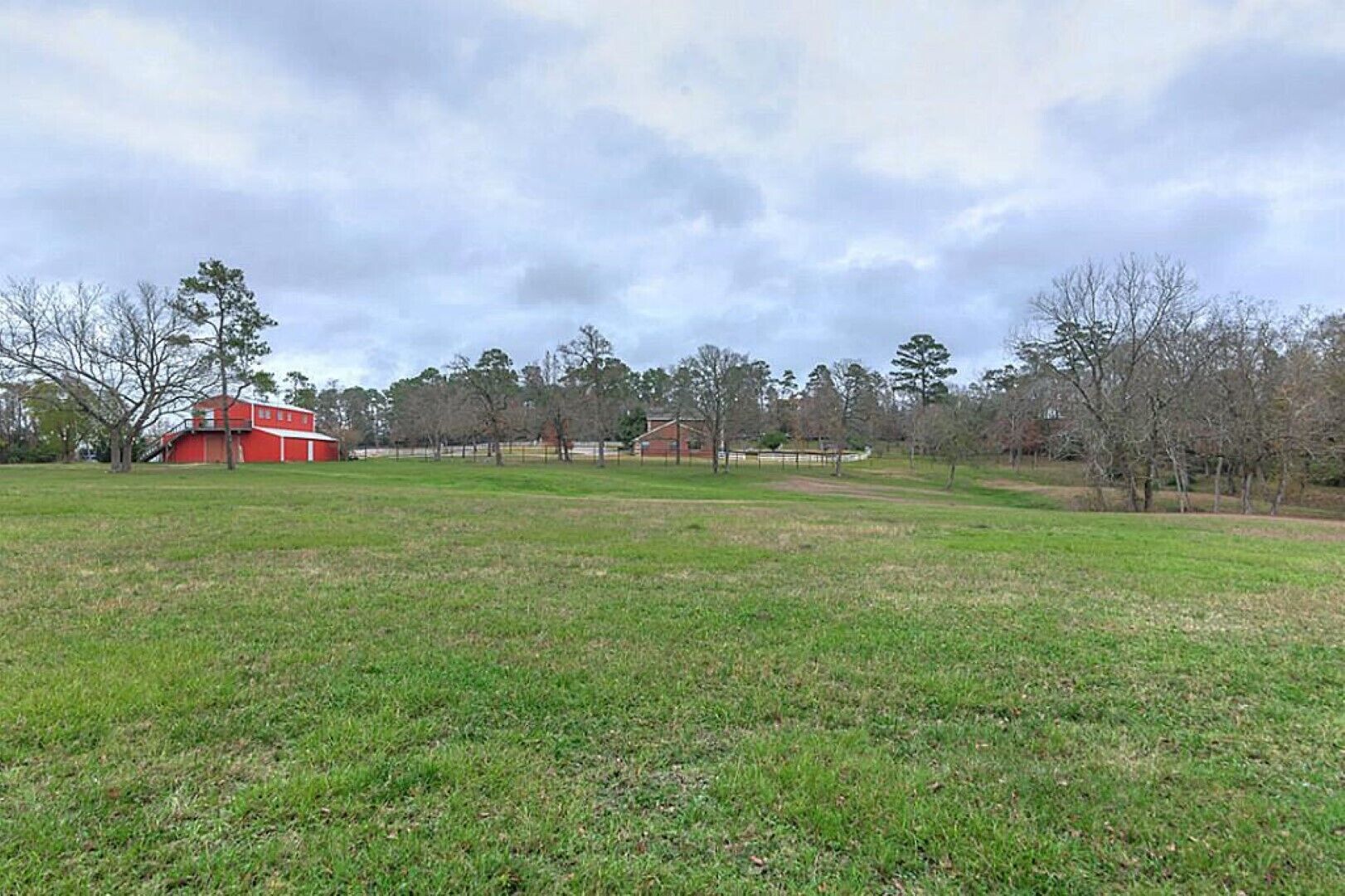 A grassy field with a red barn and a few trees.