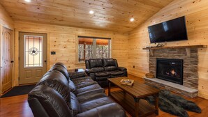 A log cabin interior with a fireplace, leather sofas, a flat-screen TV, and a stone fireplace surround. - Beautiful Private Cabin, adjacent to the National Forest (Luray)