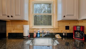 A kitchen with a granite countertop, stainless steel sink, wooden cabinets, and a window with a view of trees. - Beautiful Private Cabin, adjacent to the National Forest (Luray)