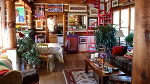A cozy cabin interior with wooden beams, a dining area, a sofa, and a staircase.