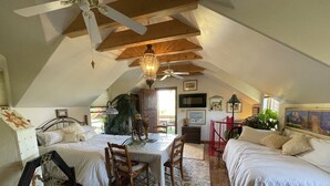 A cozy attic bedroom with two beds, a dining table, and a ceiling fan.
