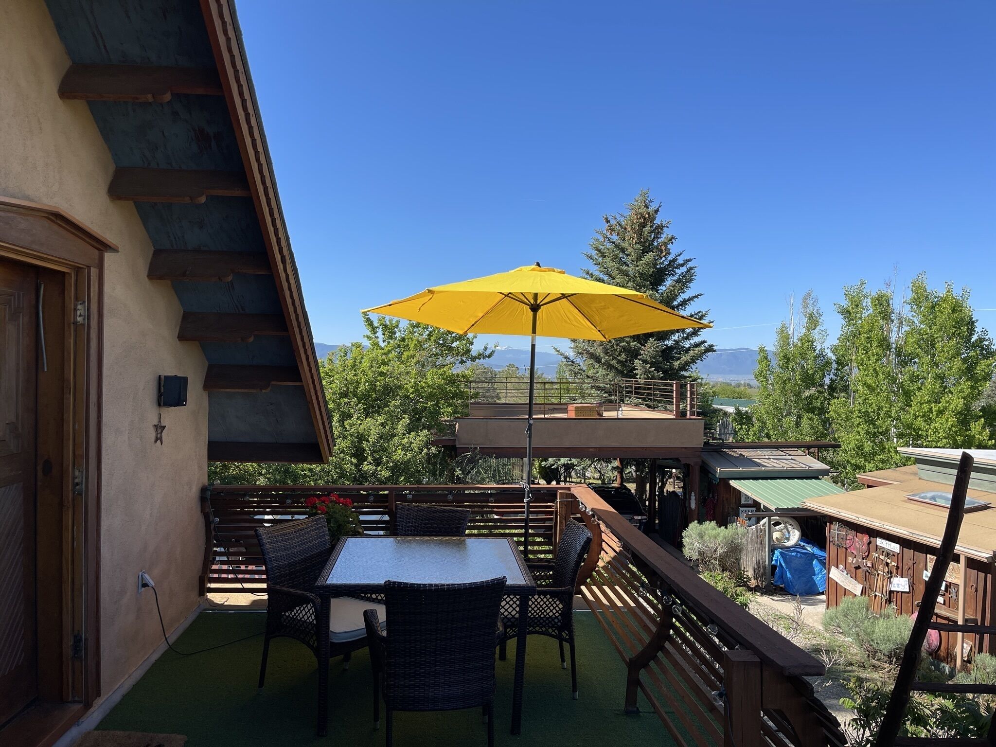 A balcony with a table and chairs, a yellow umbrella, and a view of trees and mountains.