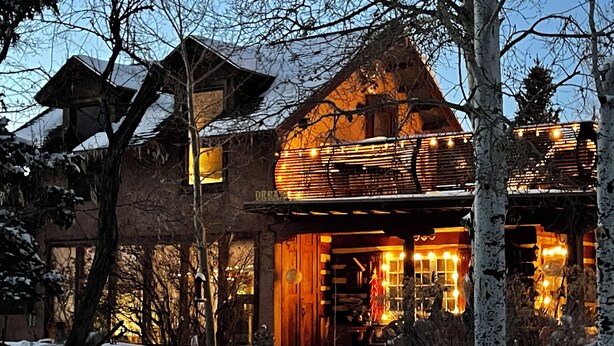 A rustic lodge with a large wooden entrance, snow-covered ground, and a snow-covered roof.