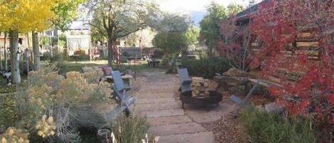 A stone pathway leading to a seating area with a fire pit, surrounded by various plants and trees.
