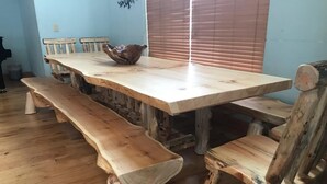 Ein rustikaler Holzesstisch mit Bänken, eine Holzwasserquelle auf dem Tisch und ein Fenster mit Jalousien im Hintergrund.