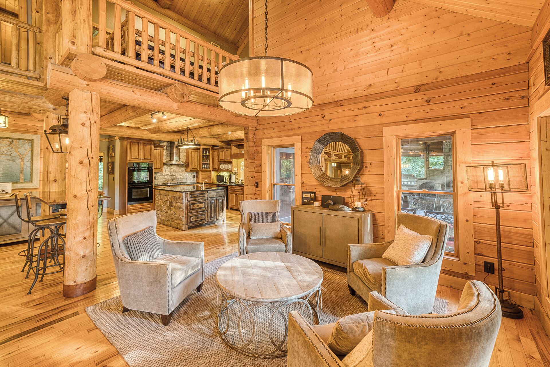 A spacious log cabin interior with a high ceiling, a central island with seating, a dining area, and a kitchen with stone accents.