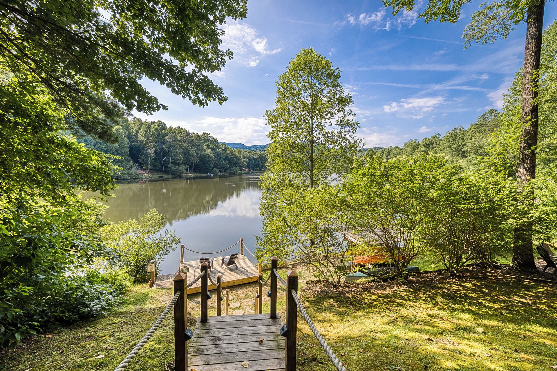 A wooden dock leading to a lake surrounded by lush greenery.