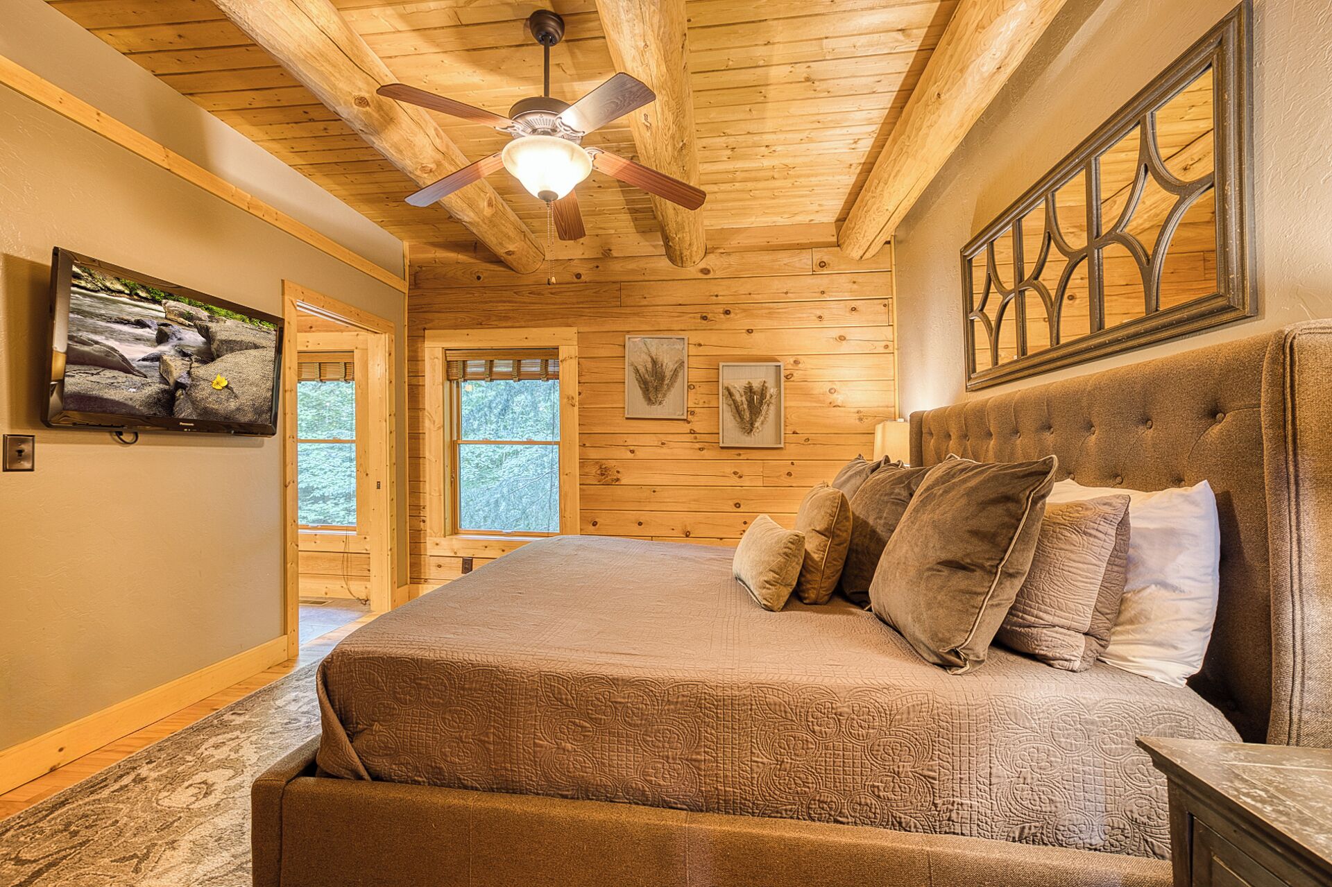 Un dormitorio con una cama grande, ventilador de techo, paredes de madera y una ventana.