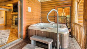 En stuga byggd av trä med ett bubbelbad, en eldstad i sten och en träveranda.